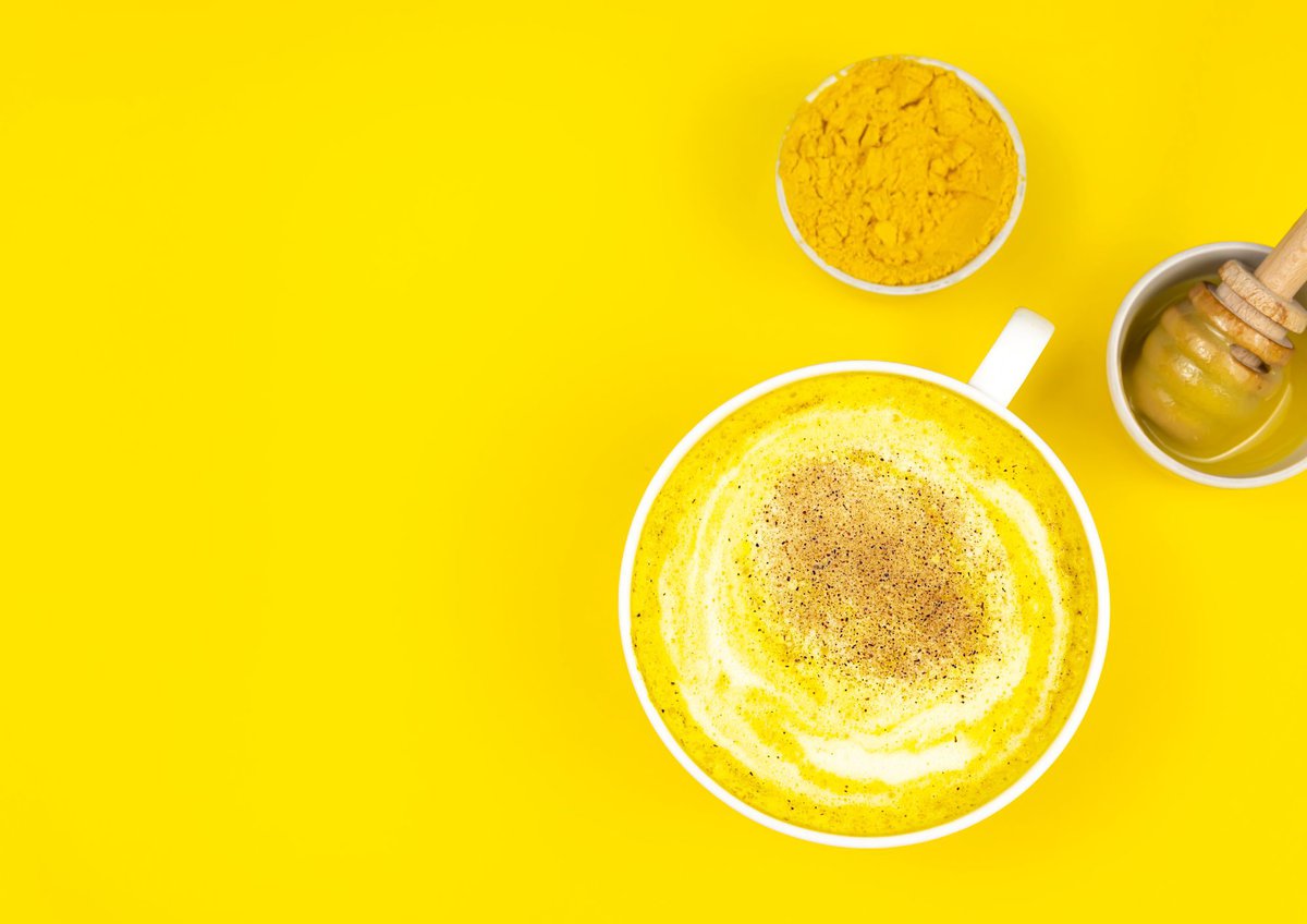 Turmeric golden milk in a mug with bright yellow background.