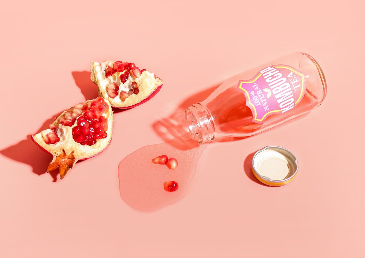 Kombucha spilled onto a pink background next to a opened pomegranate. 