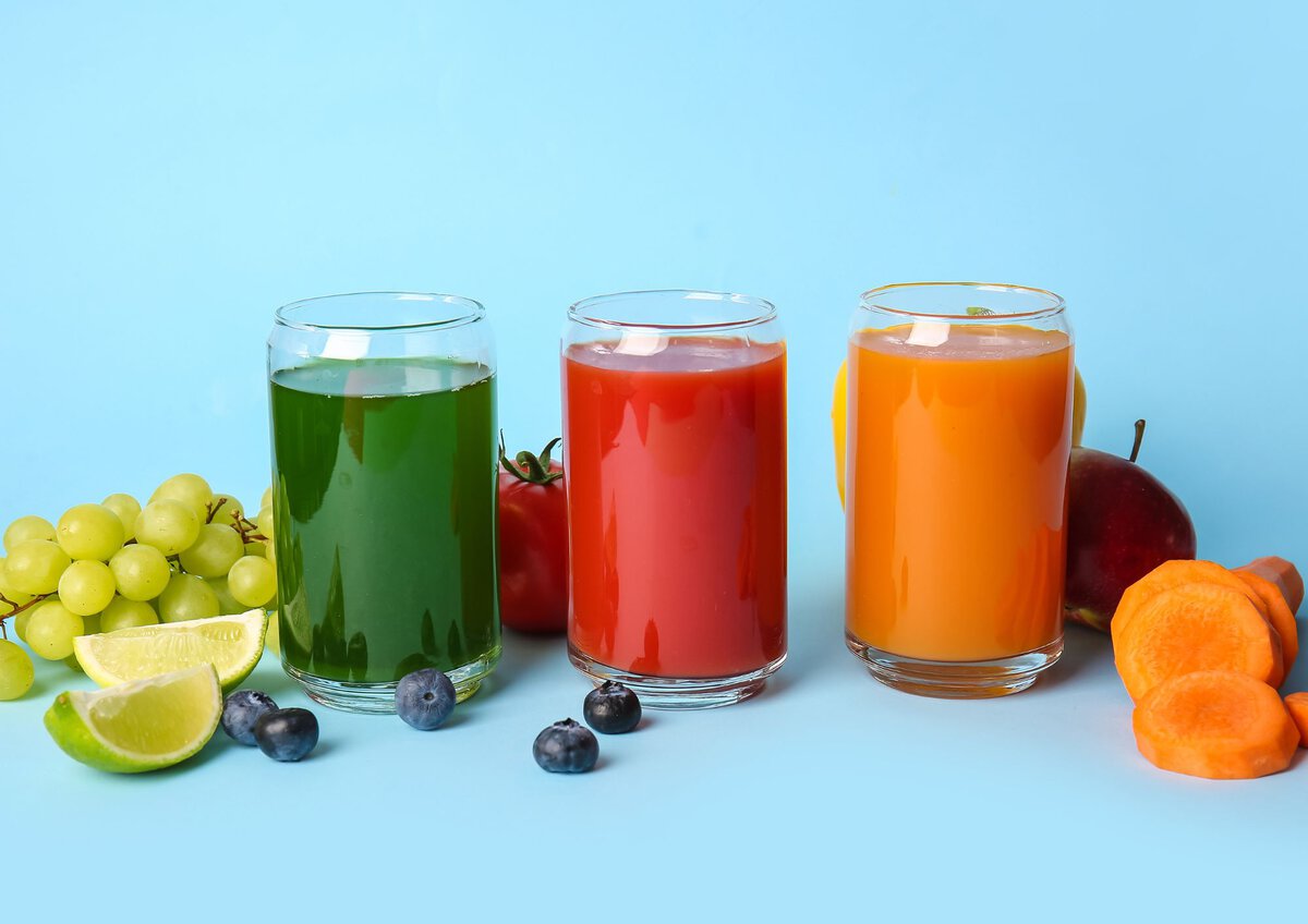 Green, red and orange juices in glasses with a blue background.