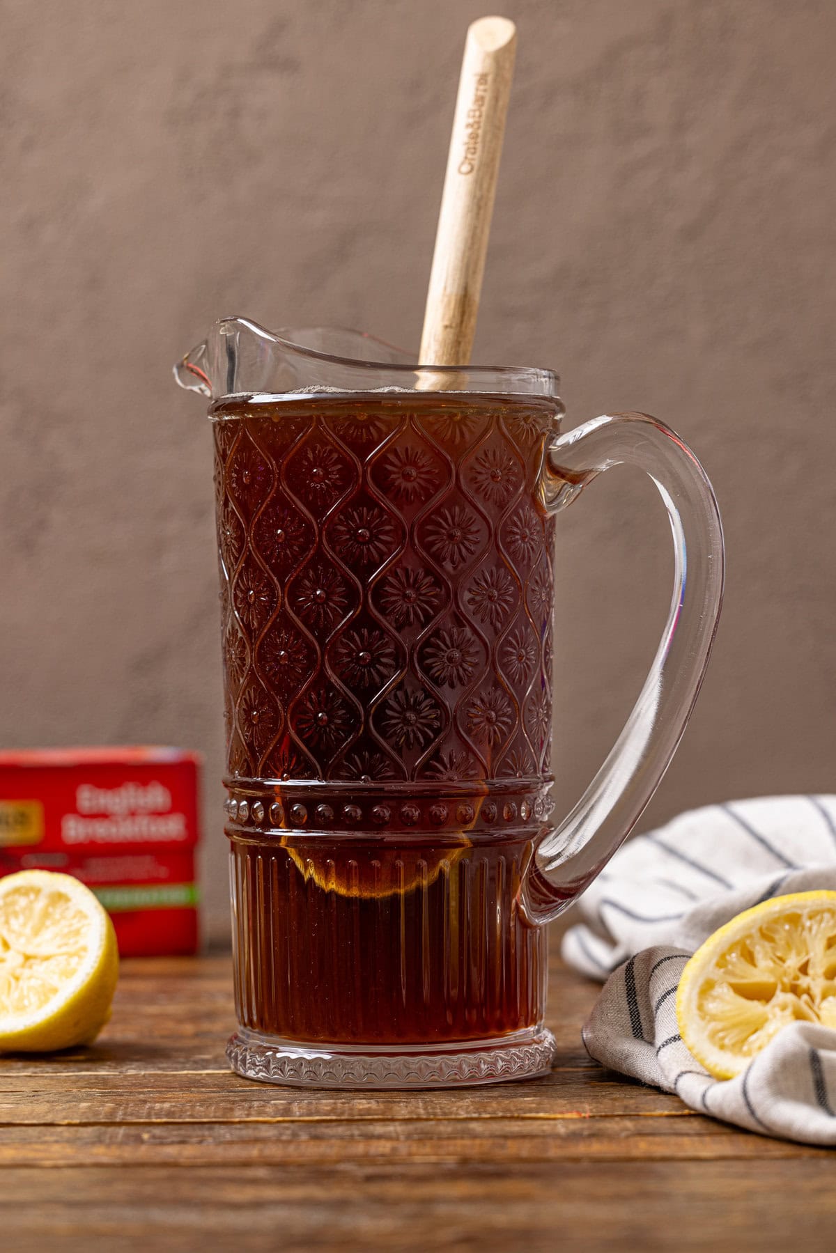 A pitcher with sweet tea and wooden spoon with lemons and black tea bags in the background. 