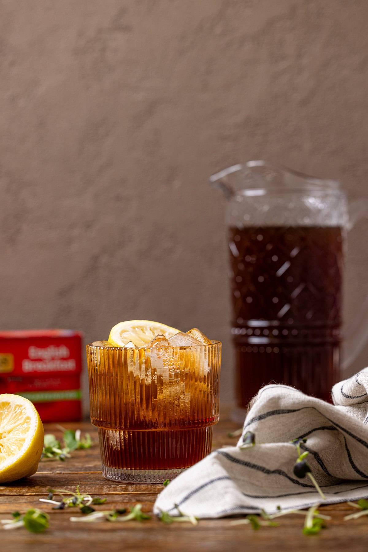 A glass of sweet tea with a lemon and a pitcher in the background. 