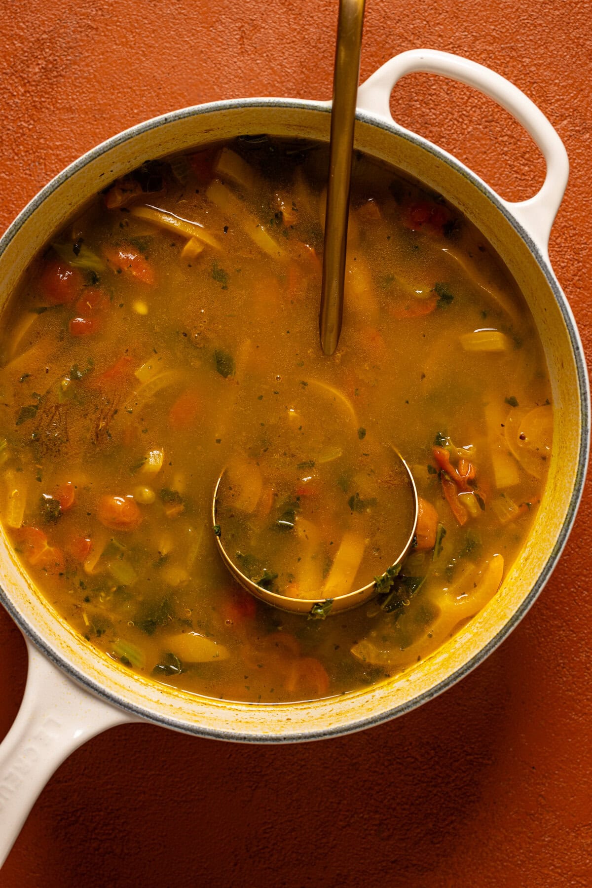 Pot of soup on a burnt orange table with a spoon.