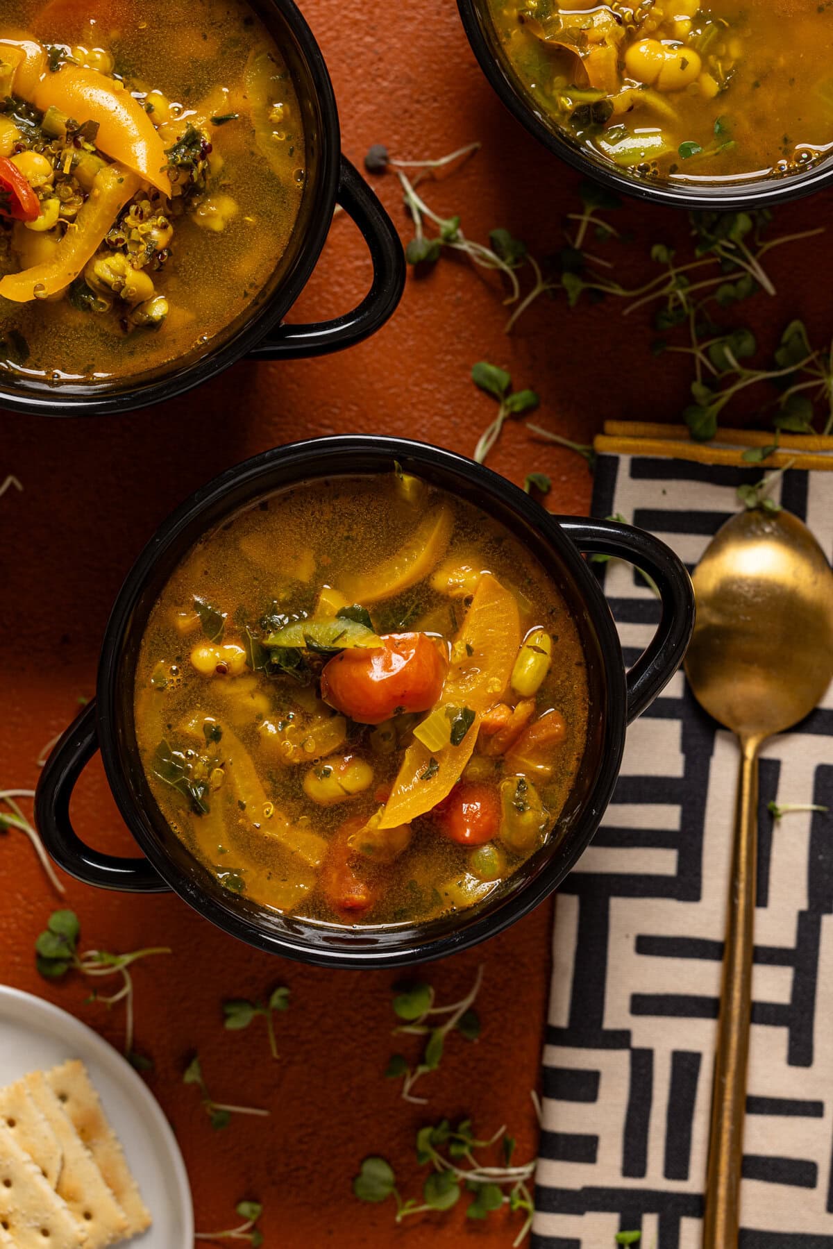 Three bowls of soup on a burnt orange table with a spoon.