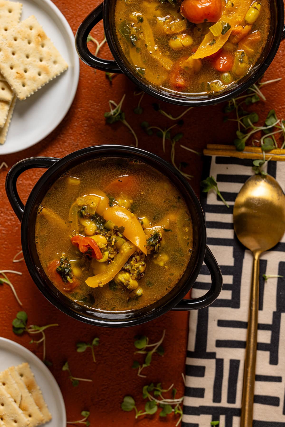 Two bowls of soup with a spoon and crackers. 