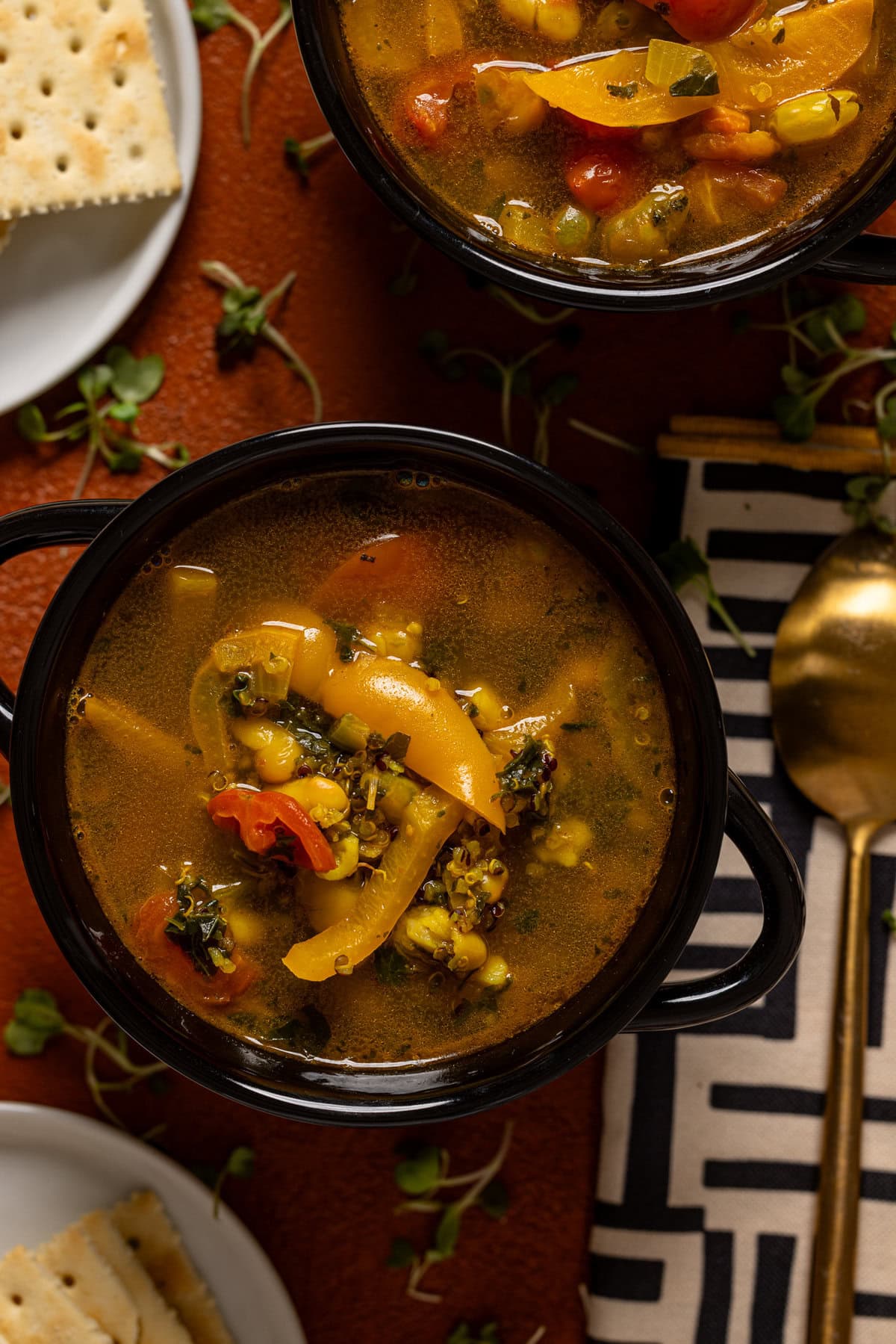 Two bowls of soup with a spoon with a side of crackers.