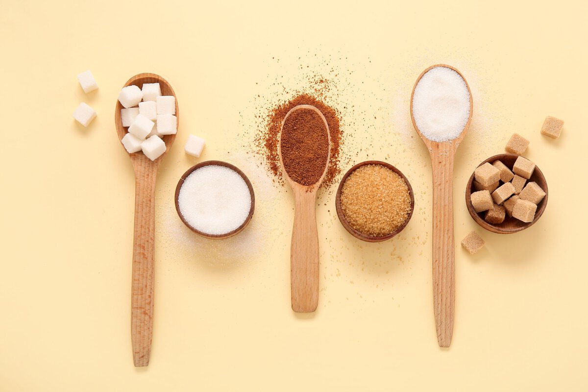 Different types of sugar in wooden spoons and bowls on yellow background.