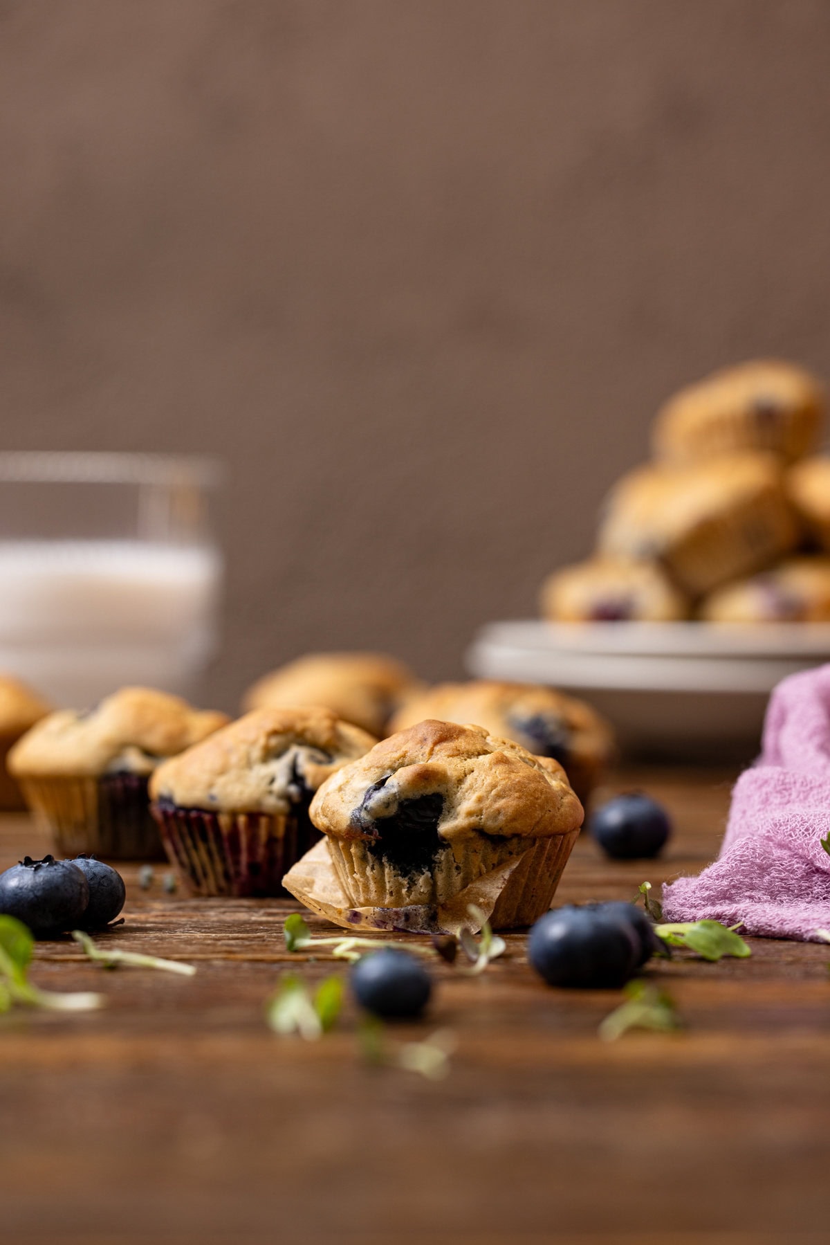 Blueberry muffins on a brown wood table with a glass of milk.