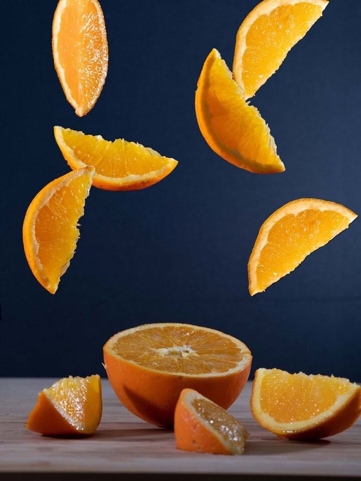 Sliced oranges in the air and on a table.