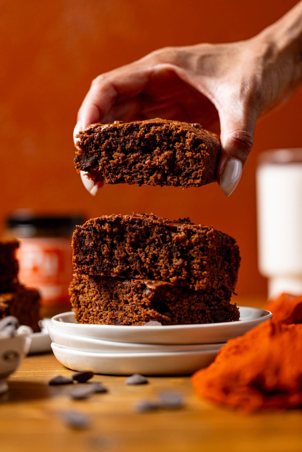 Hand of Shanika lifting a brownie from a stack on white plates.