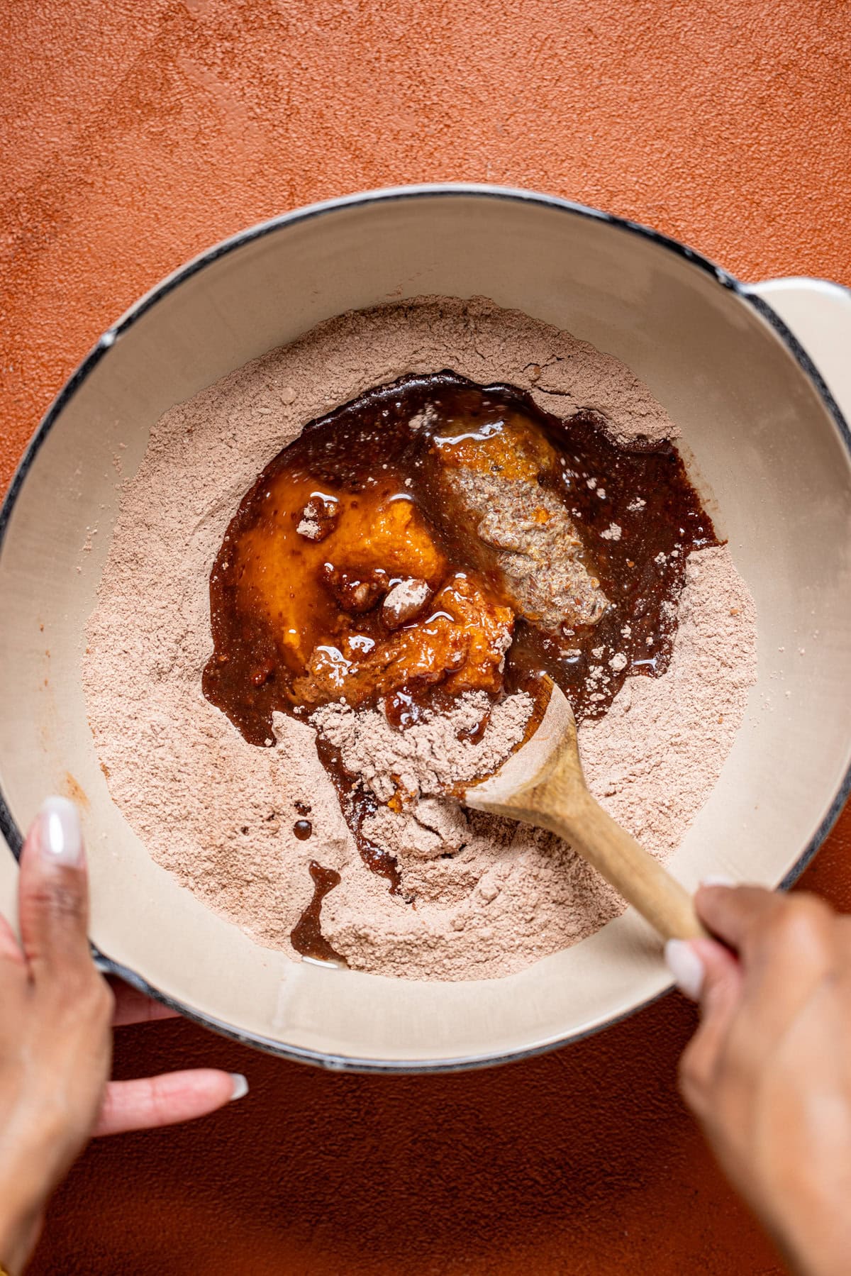 All brownie ingredients being stirred with a wooden spoon in a bowl.