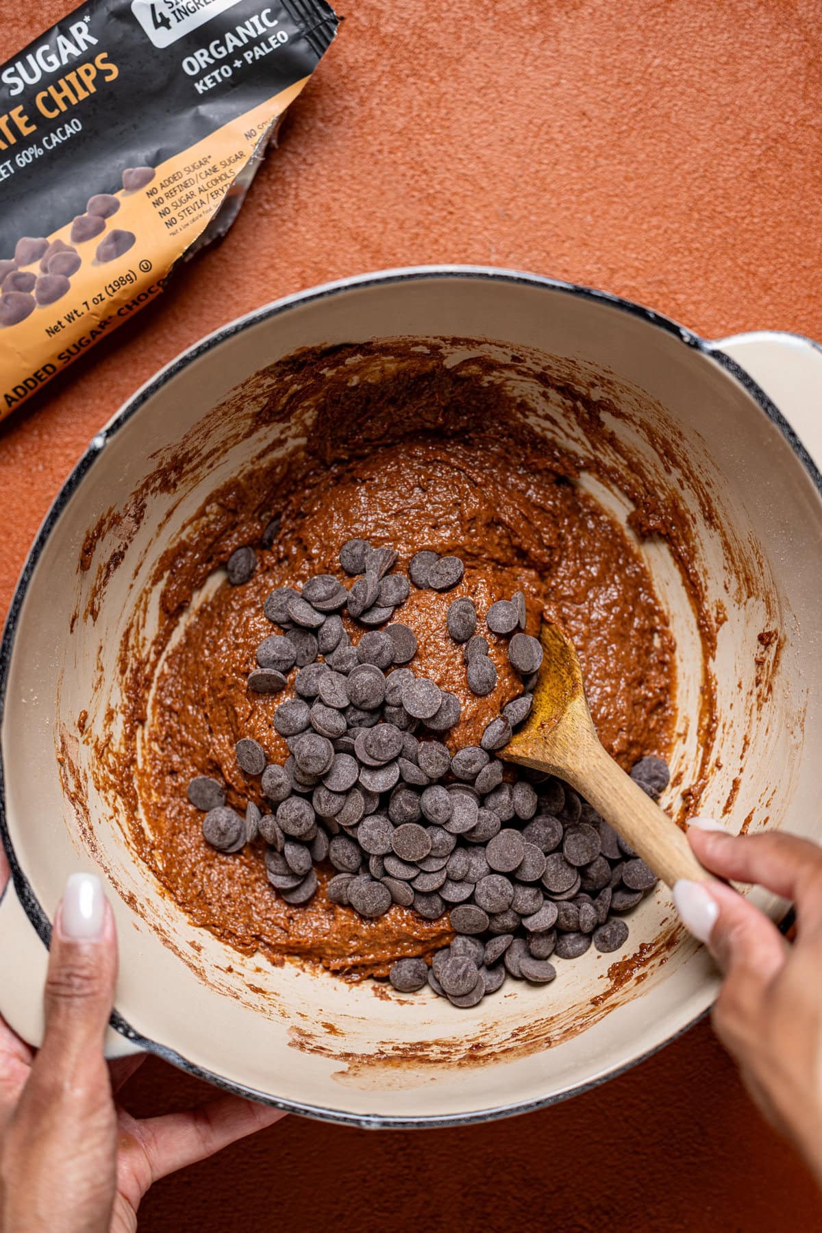 Chocolate chips being stirred in brownie batter in a bowl.