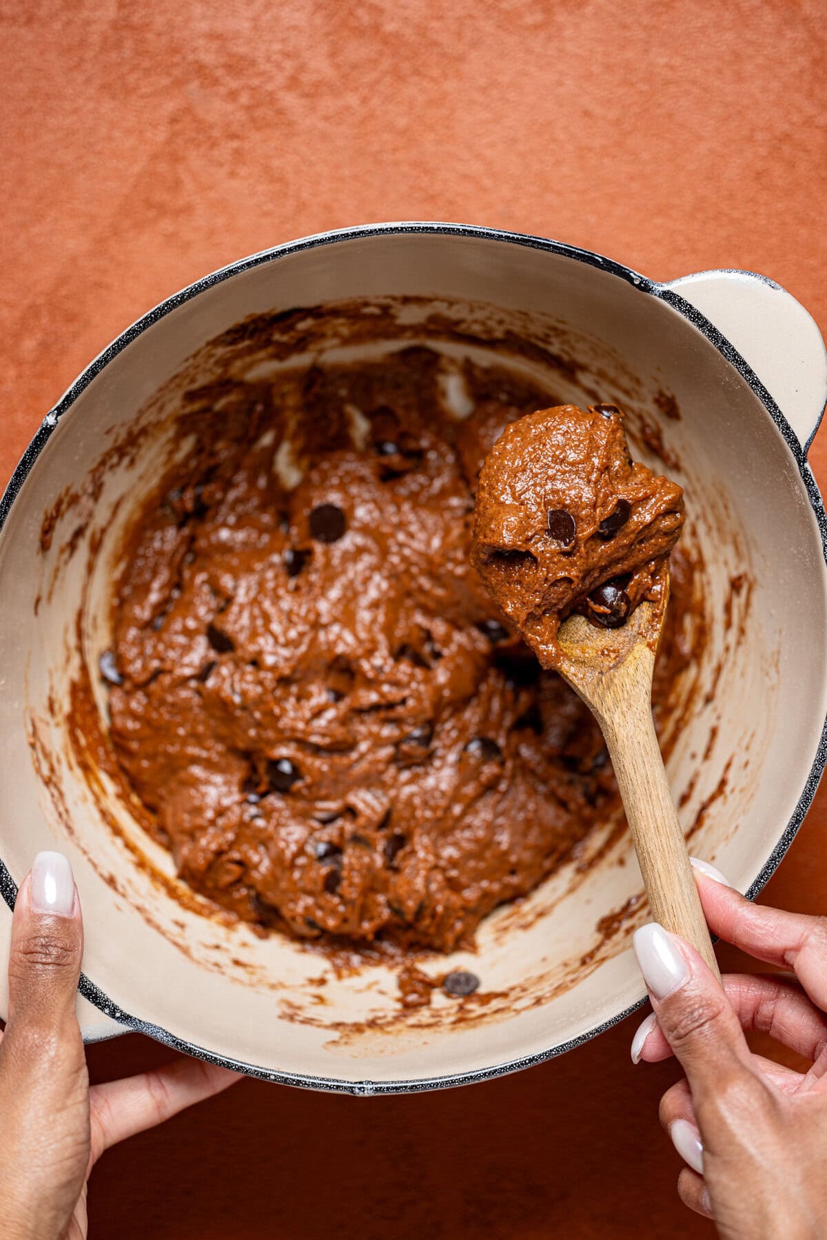 Brownie batter being stirred in a bowl with a wooden spoon.