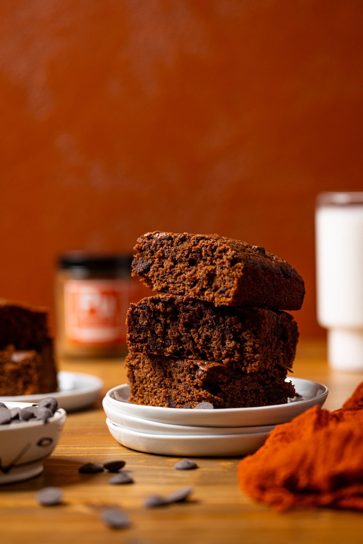 Stacks of sweet potato brownies on a white plates with a glass of milk and chocolate chips.