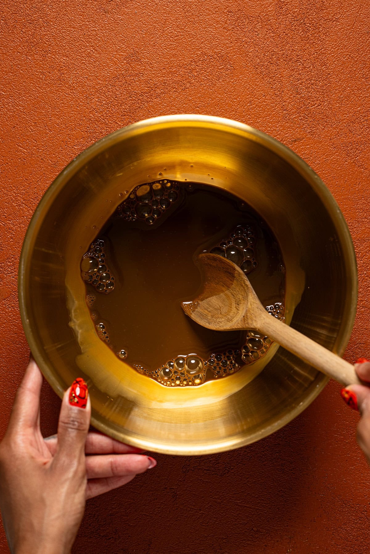 Molasses mixture in a gold bowl being stirred with a wooden spoon.