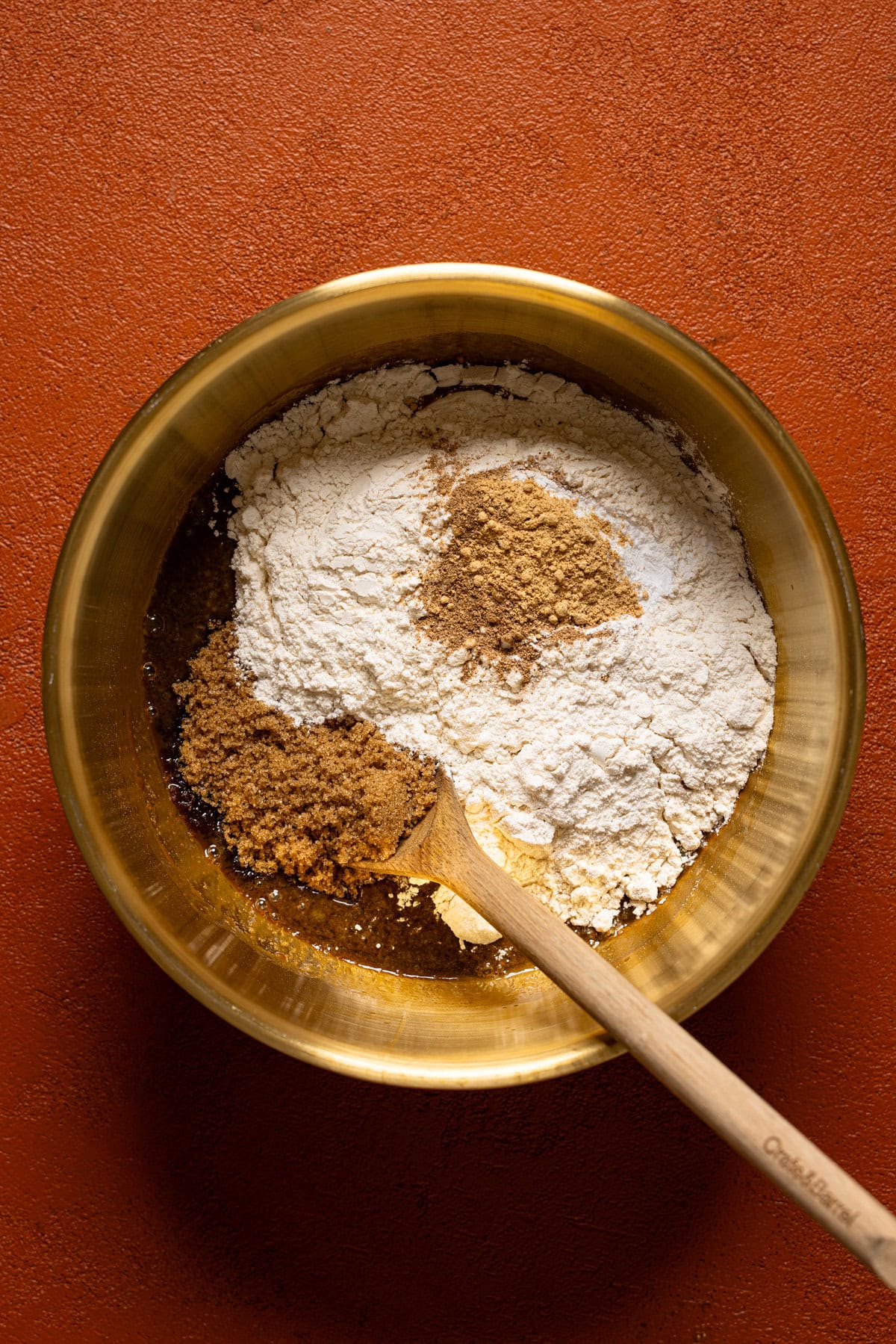 Muffin ingredients together in a gold bowl with a wooden spoon.