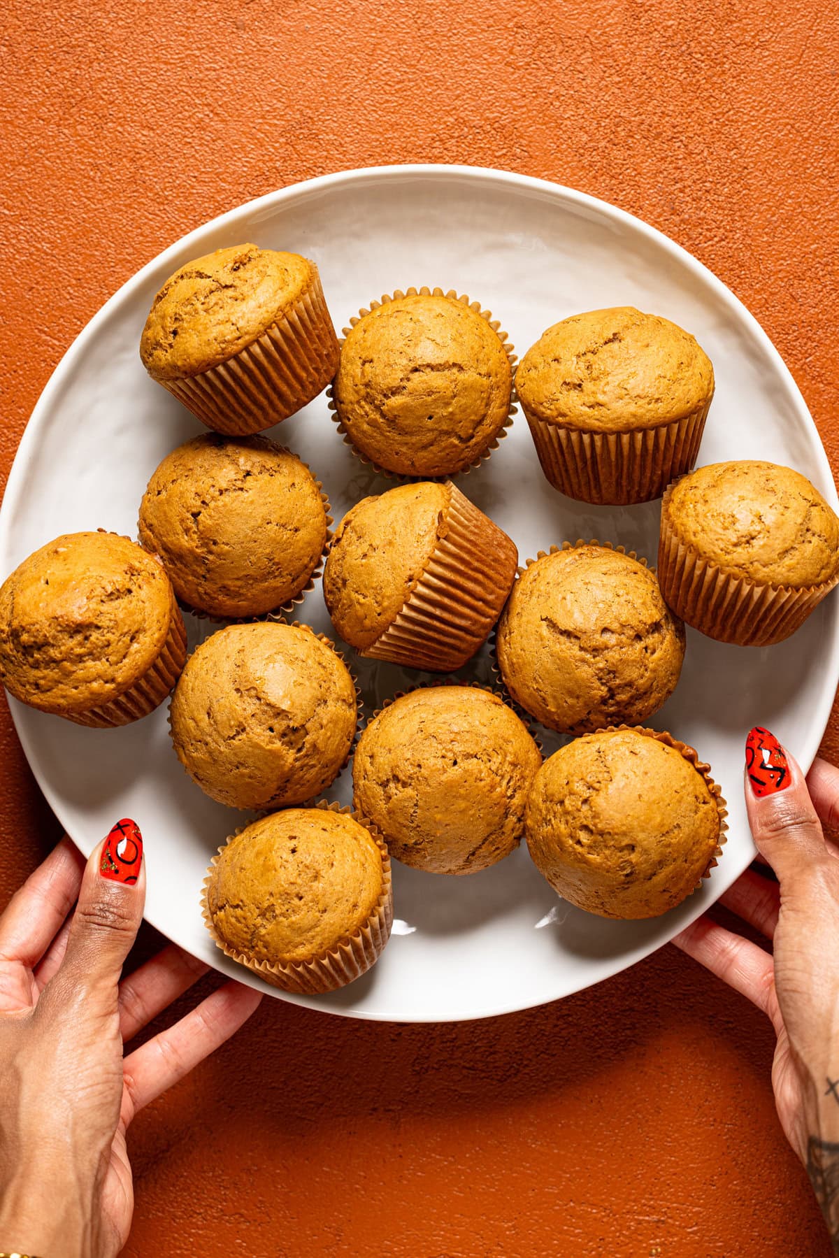 Baked muffins in a white platter being held with hands.