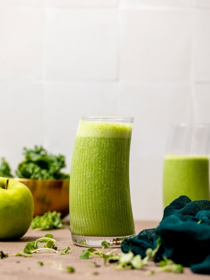 Green smoothie in a glass with apples and kale in background.