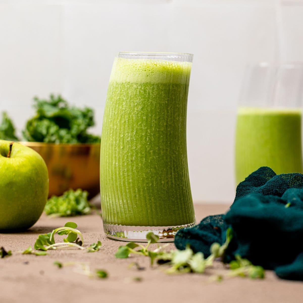 Green smoothie in a glass with apples and kale in background.