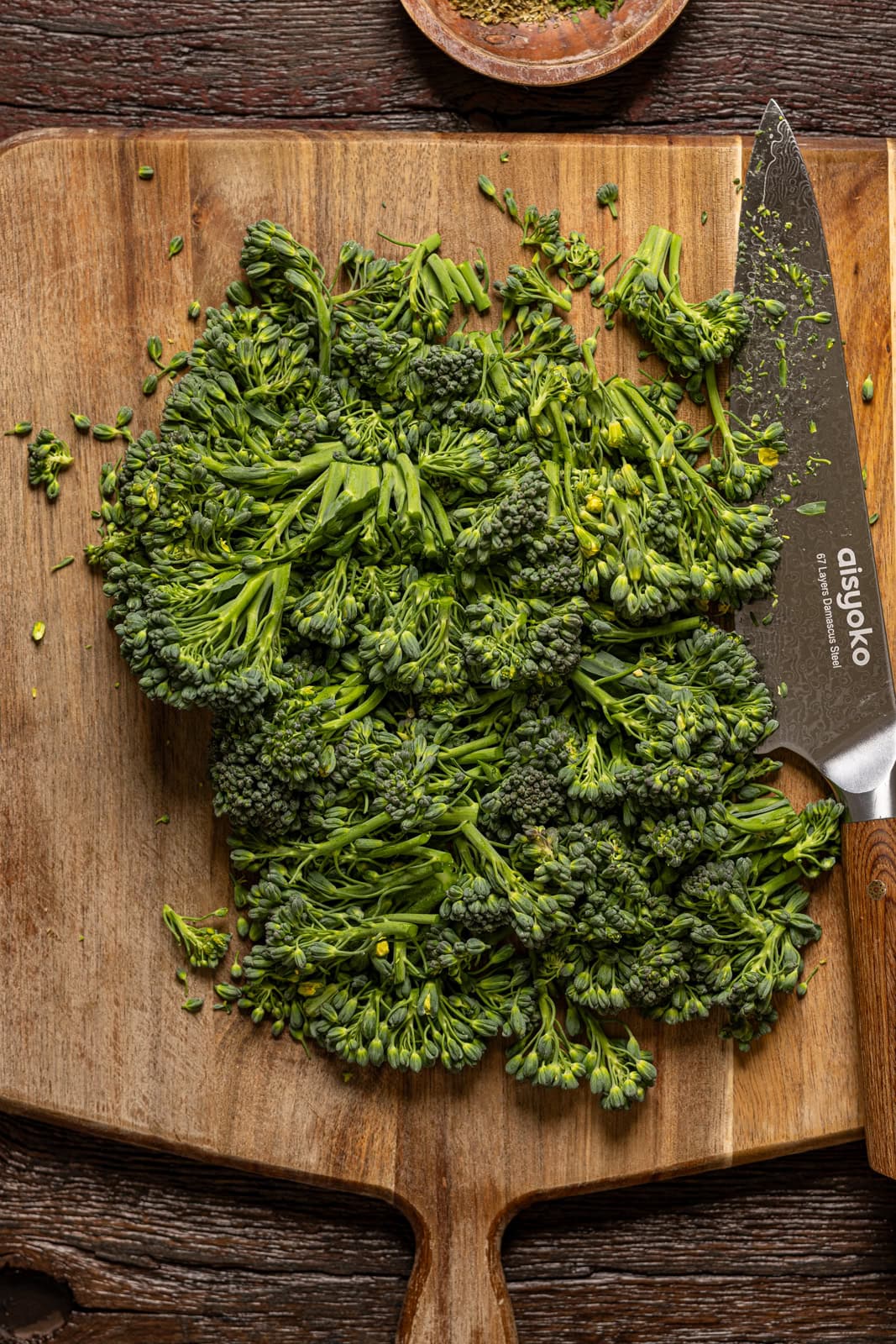 Chopped broccolini on a cutting board with a knife.