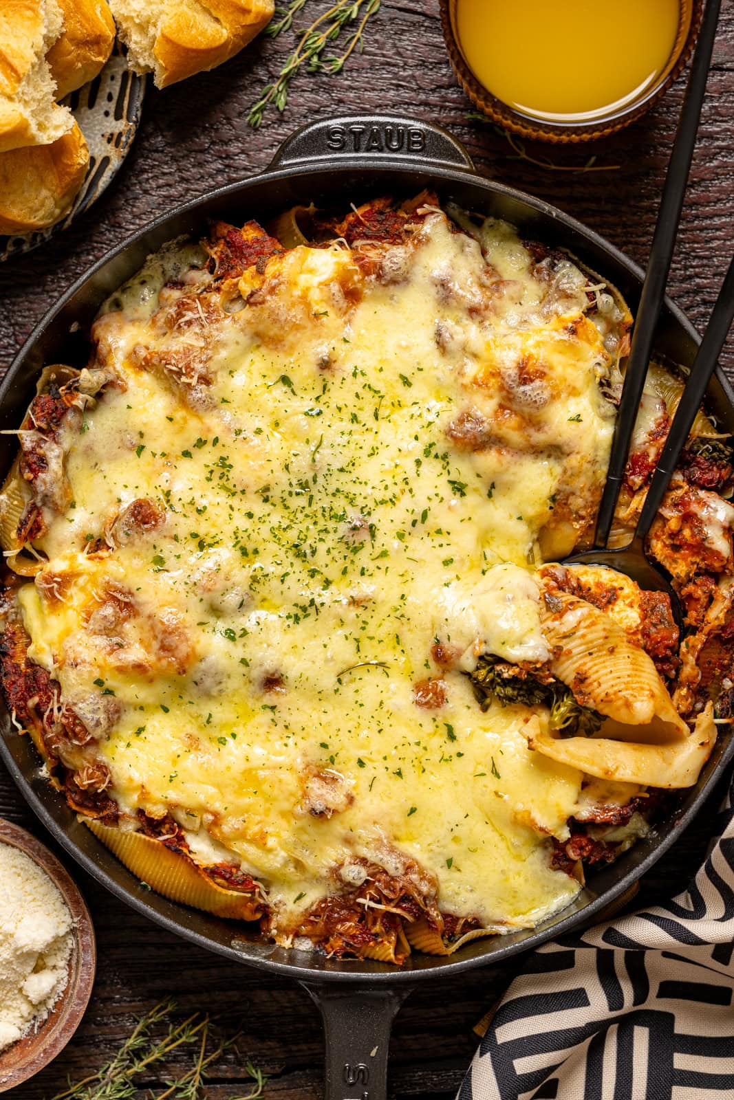 Stuffed shells in a skillet with a side of parmesan and a drink.