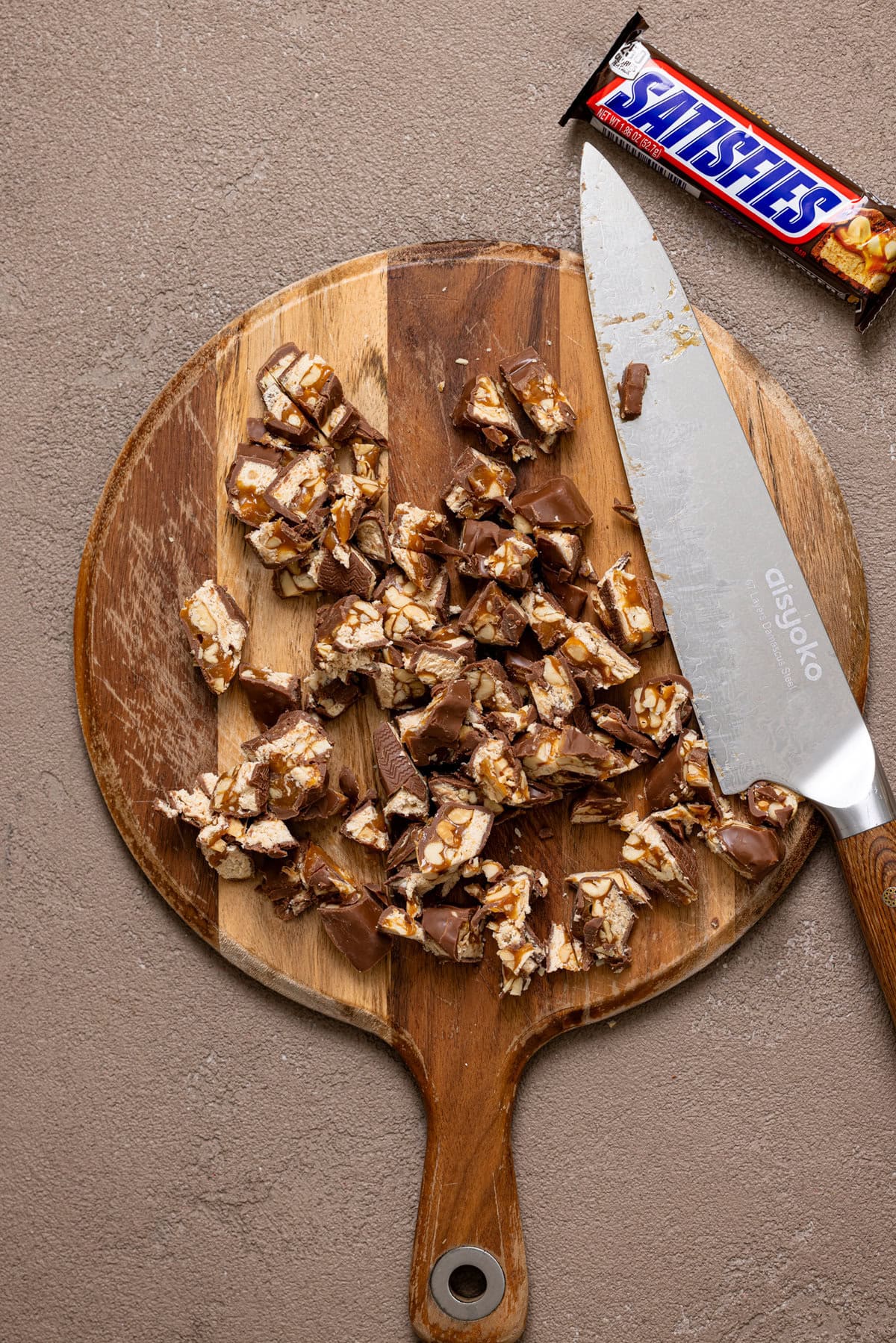 Chopped Snickers Bar candy on a cutting board with a knife.
