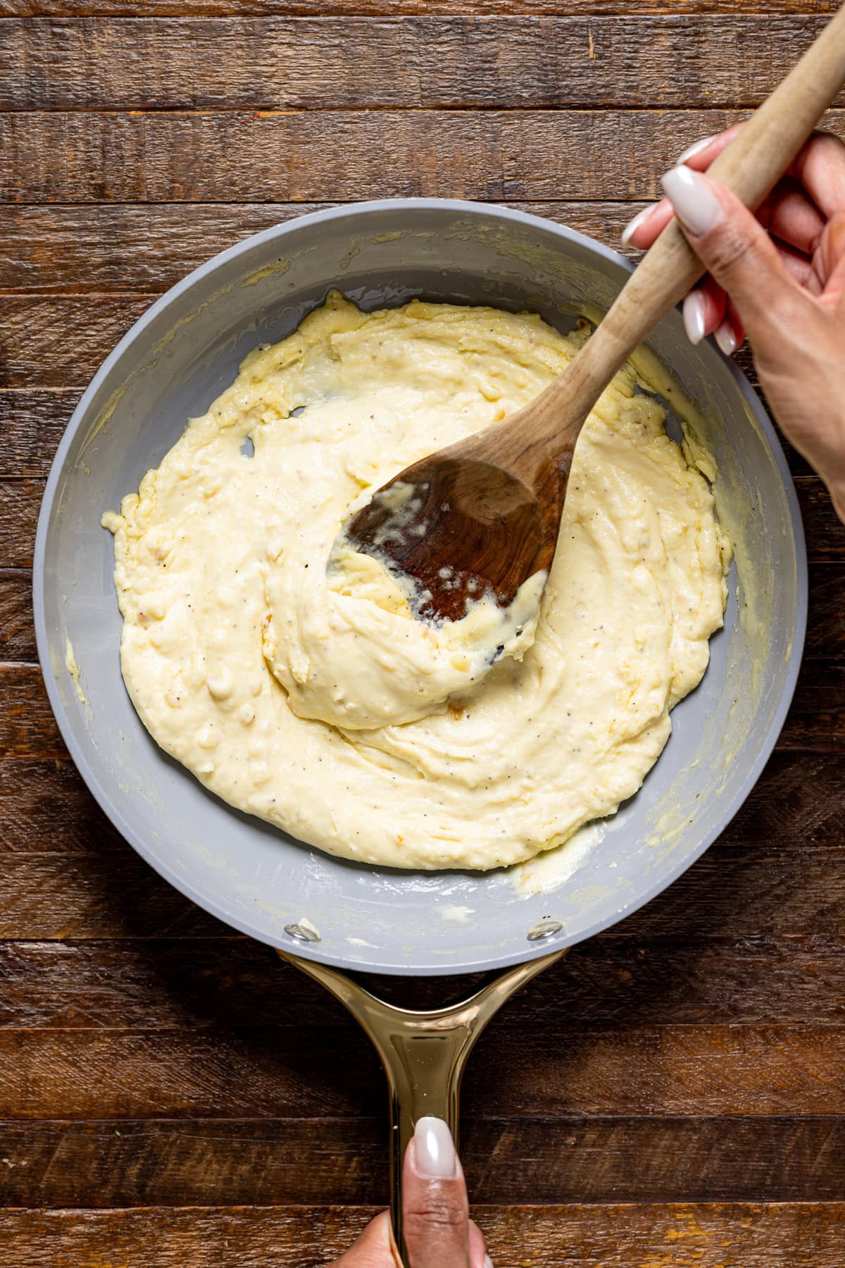 Garlic parmesan sauce in a skillet being held with a wooden spoon.