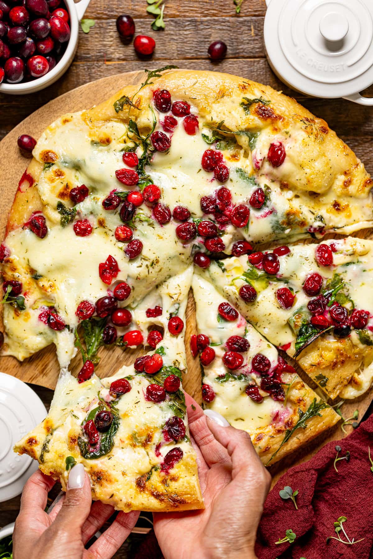 A female hand holding a slice of pizza with cranberries.