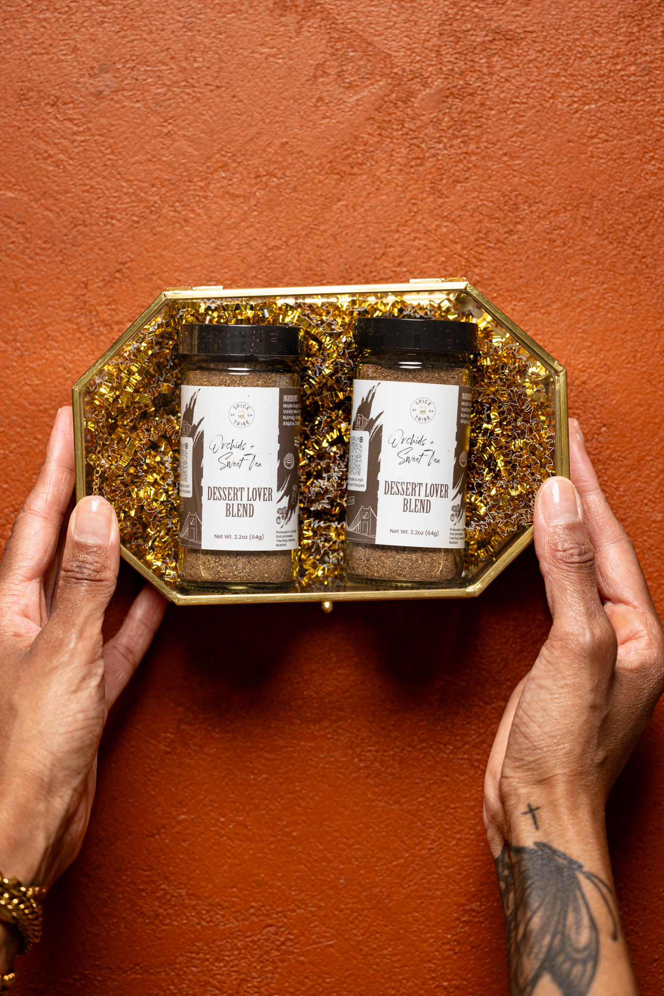 Spice blends in a gold container being held by hands on a burnt orange table.