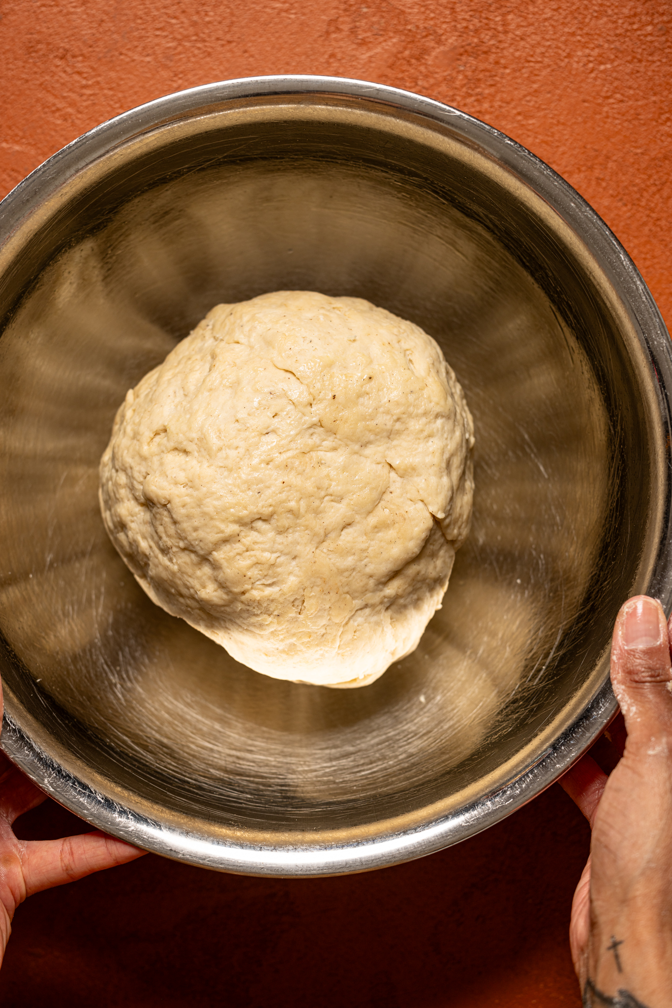 Cinnamon roll dough being held in a silver bowl.