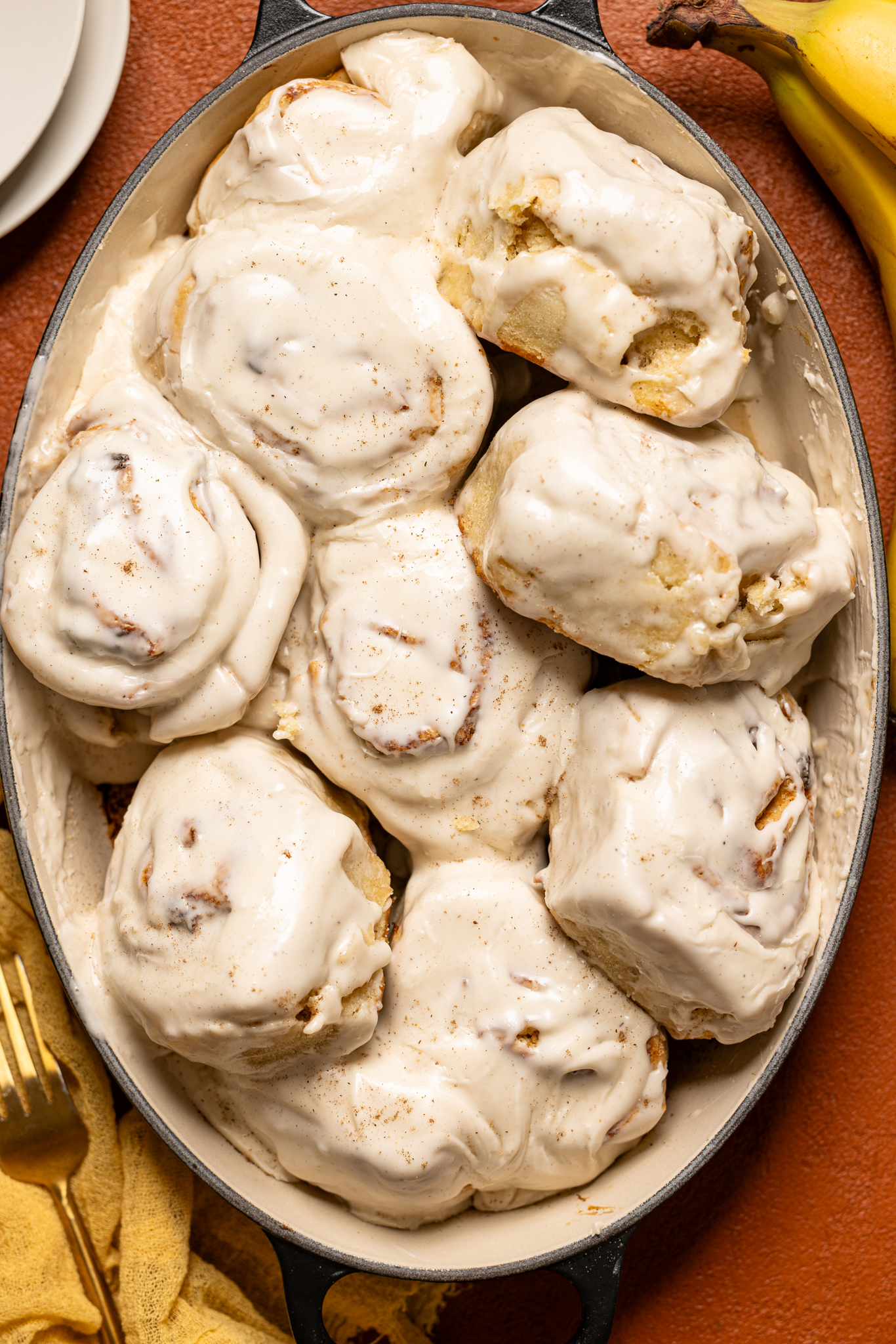 Banana Bread Cinnamon Rolls in a baking dish with a banana and plates on the side.