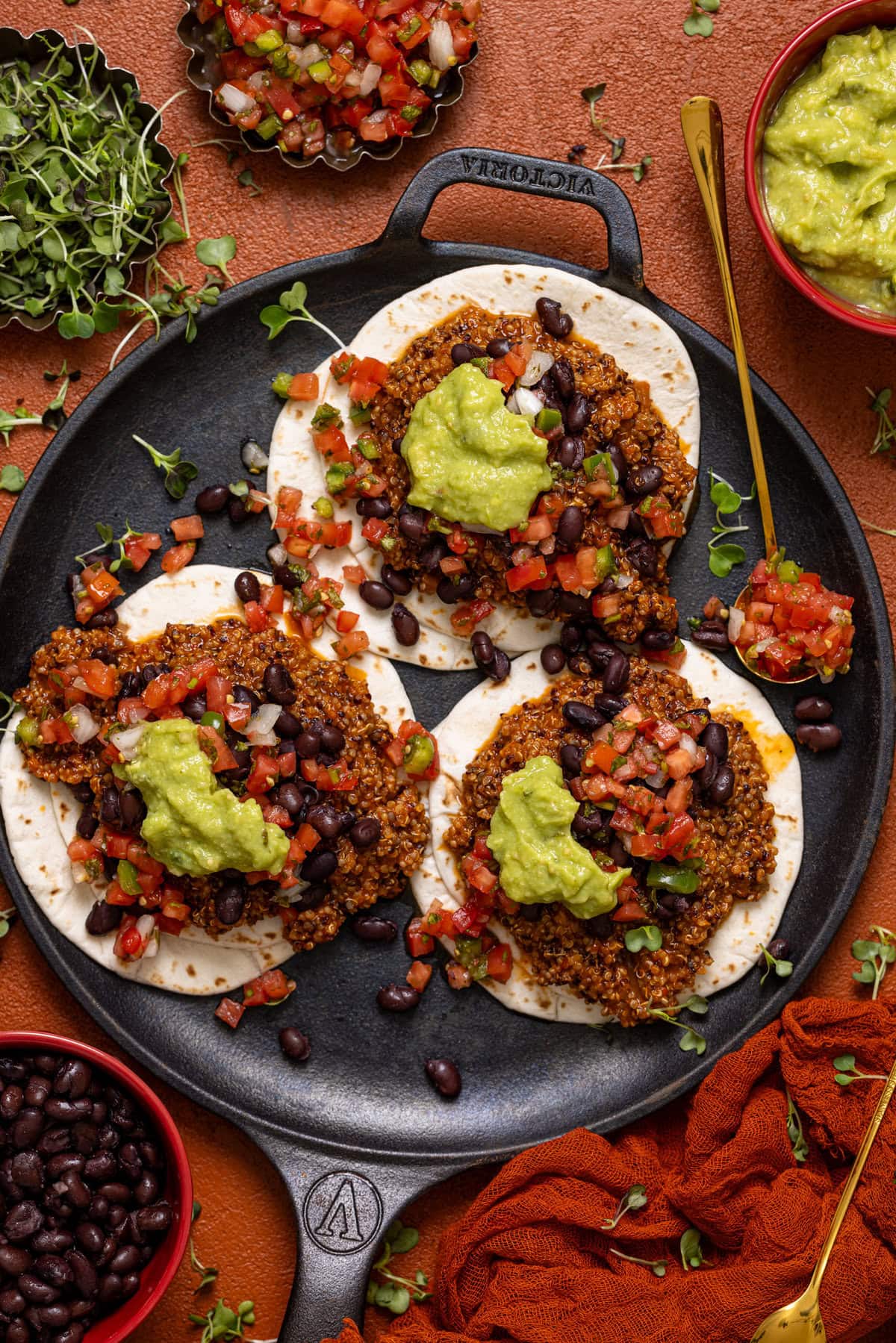 Tacos on a black low skillet with a spoon and toppings.