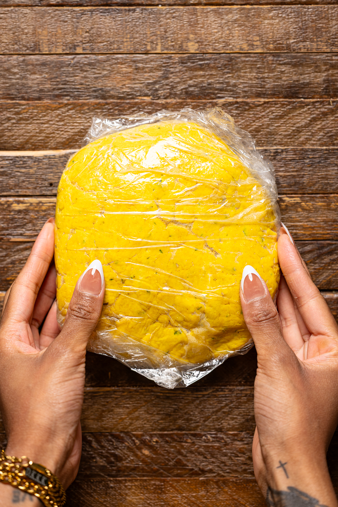 Image of Shanika's hands holding the patty crust dough wrapped in plastic wrap.