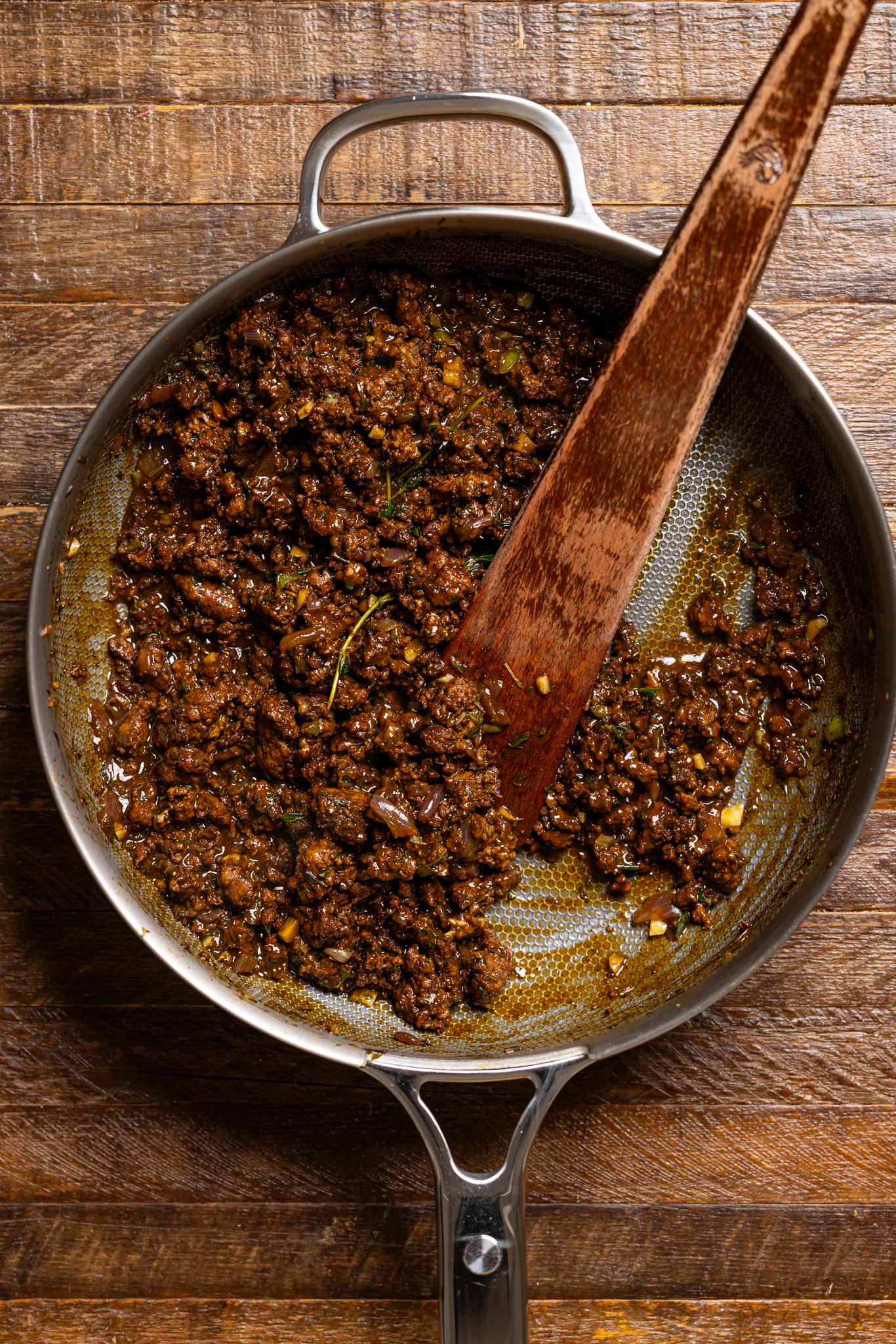 Ingredients of cooked patty filling in a skillet with a wooden spoon.