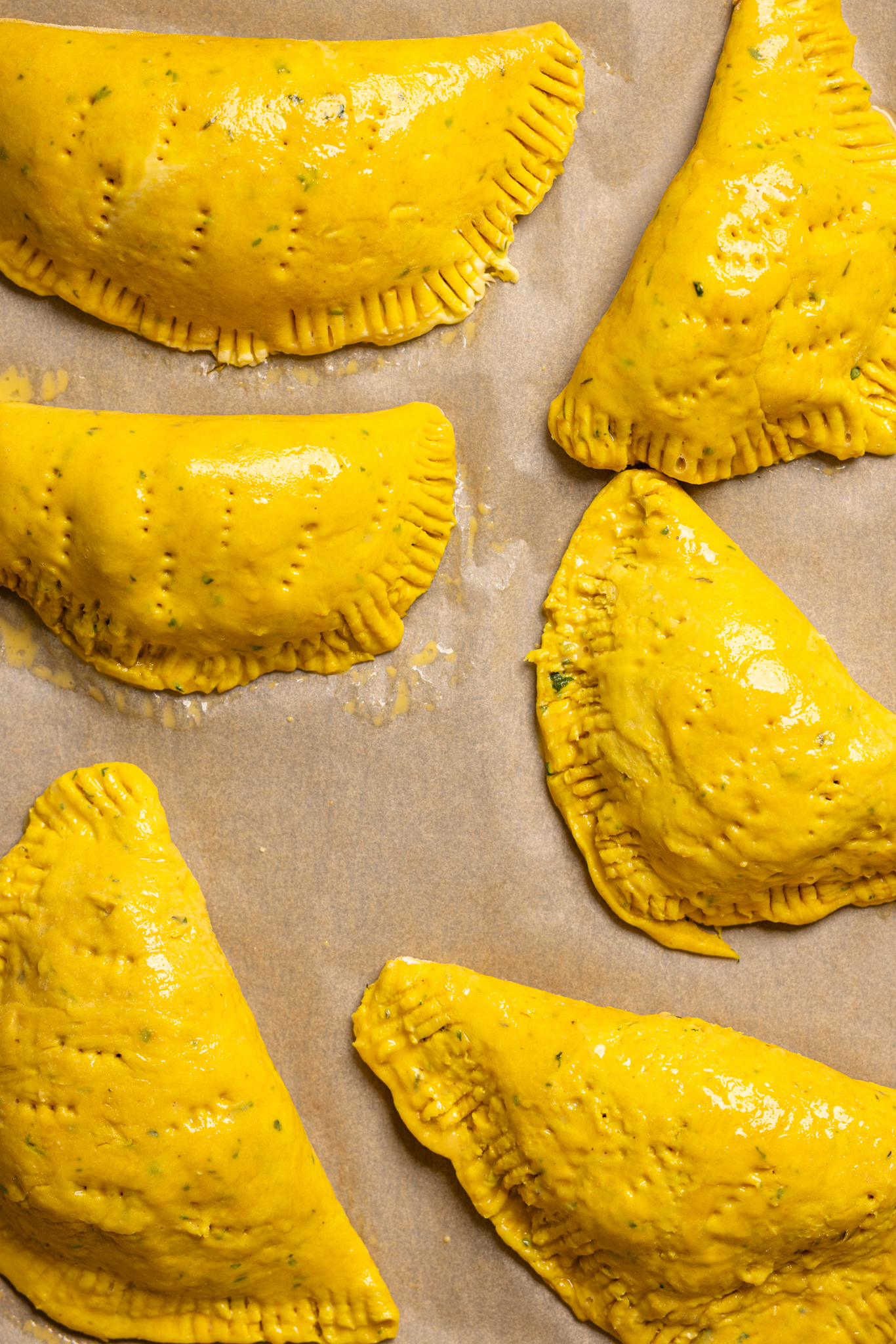 Image of Jamaican patties assembled on a baking sheet with parchment paper.