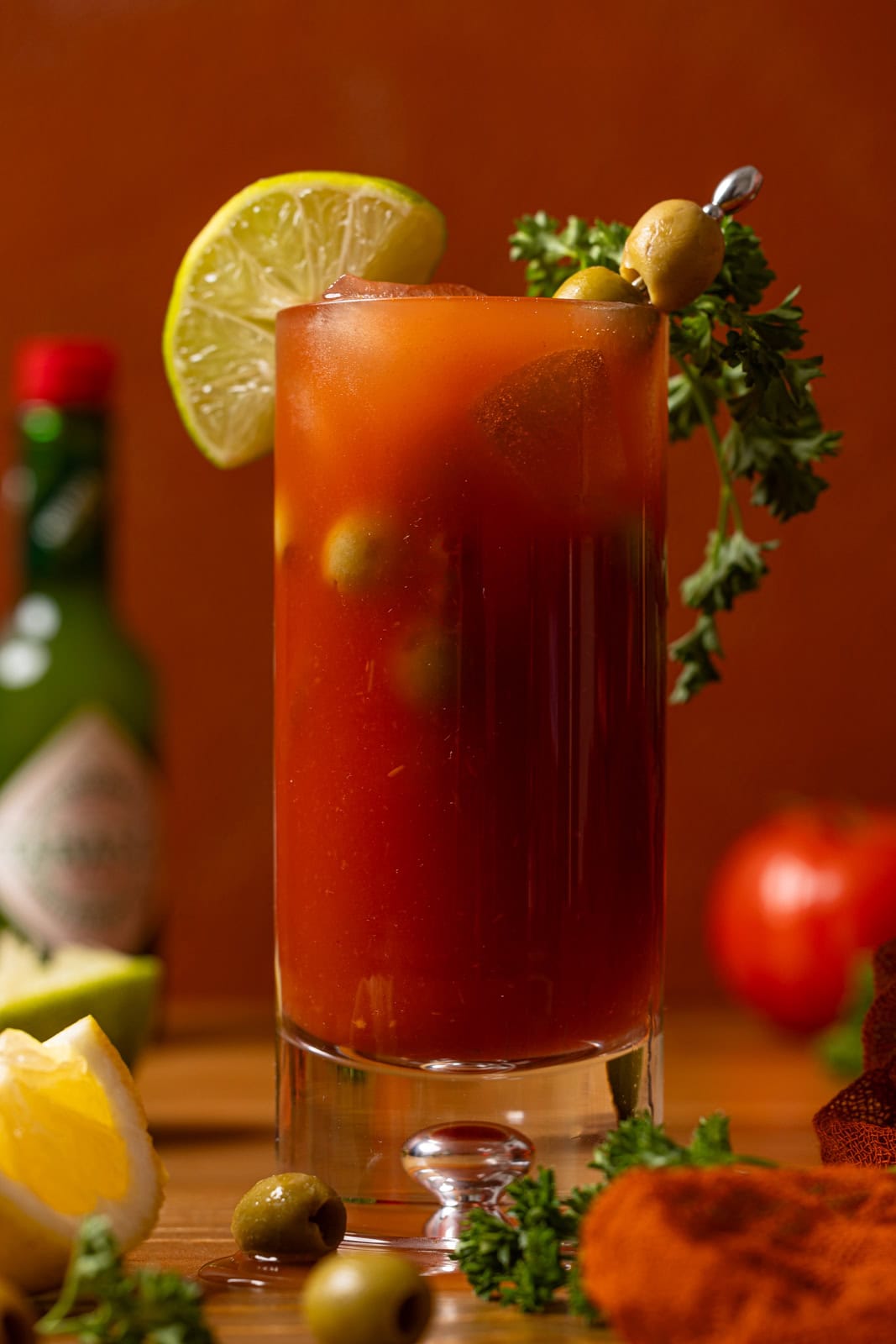 Up close shot of mocktail with lime, olives, parsley, and tobascco sauce in background.