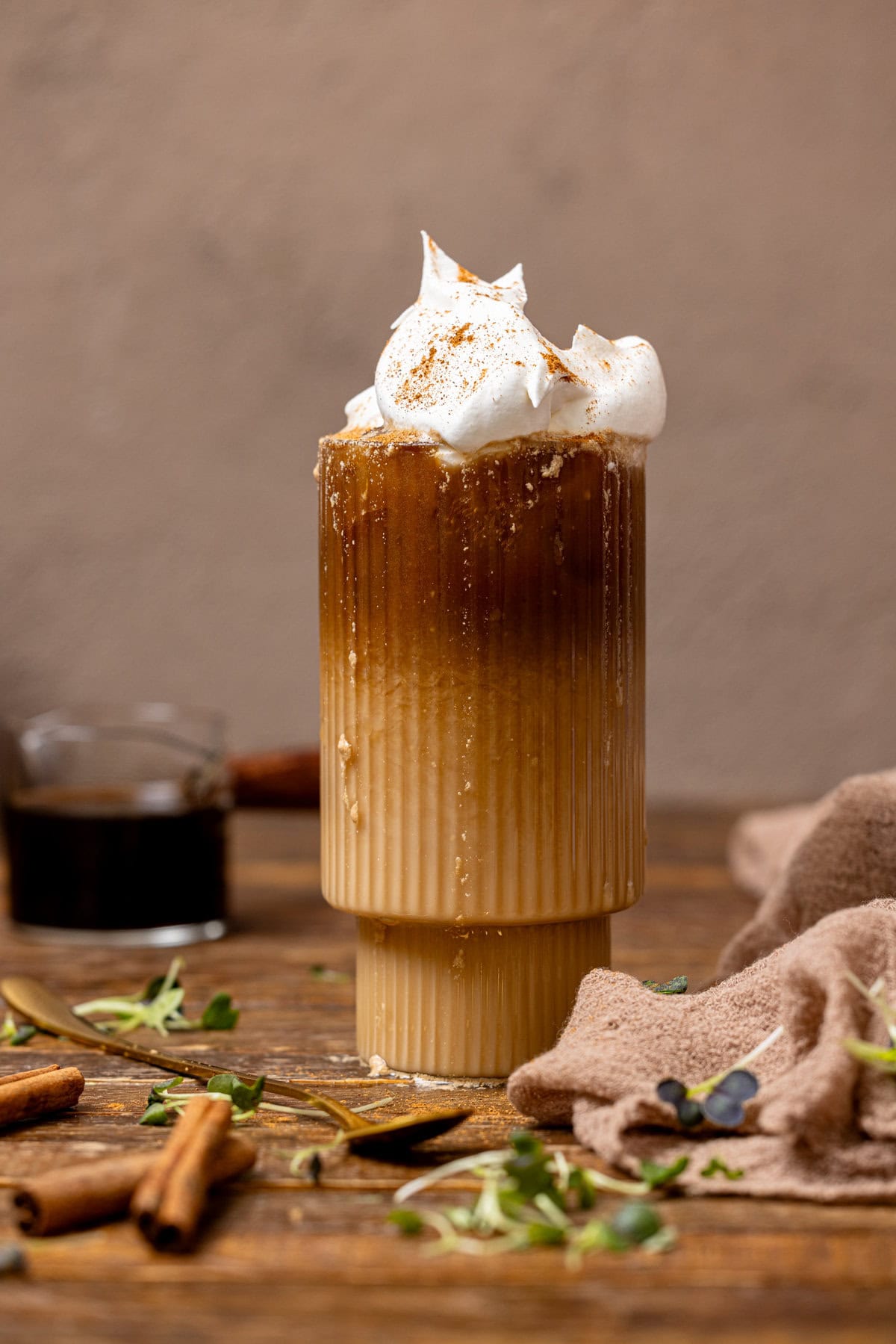 Dirty chai latte in a glass with brewed coffee in the background with cinnamon sticks.