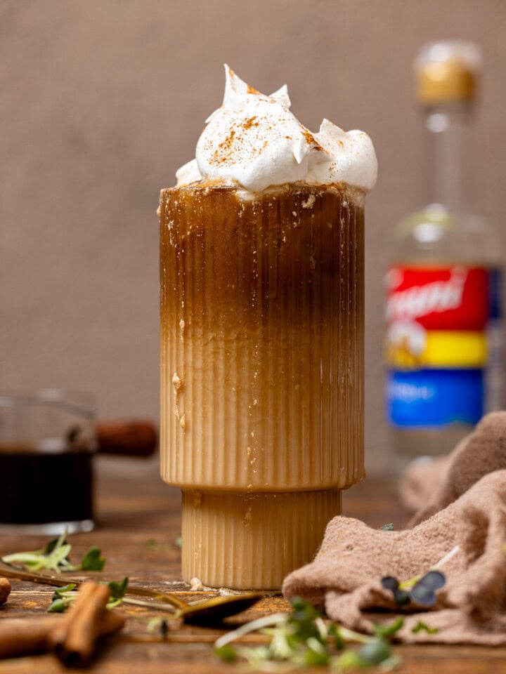 Dirty chai latte in a glass with brewed coffee and vanilla syrup in background.