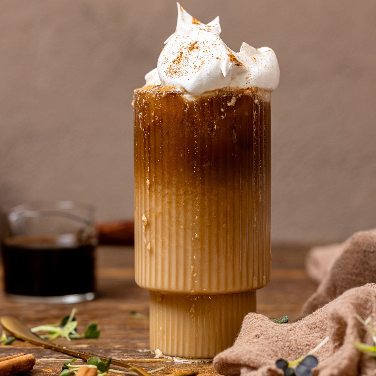 Dirty chai latte in a glass with brewed coffee in the background with cinnamon sticks.