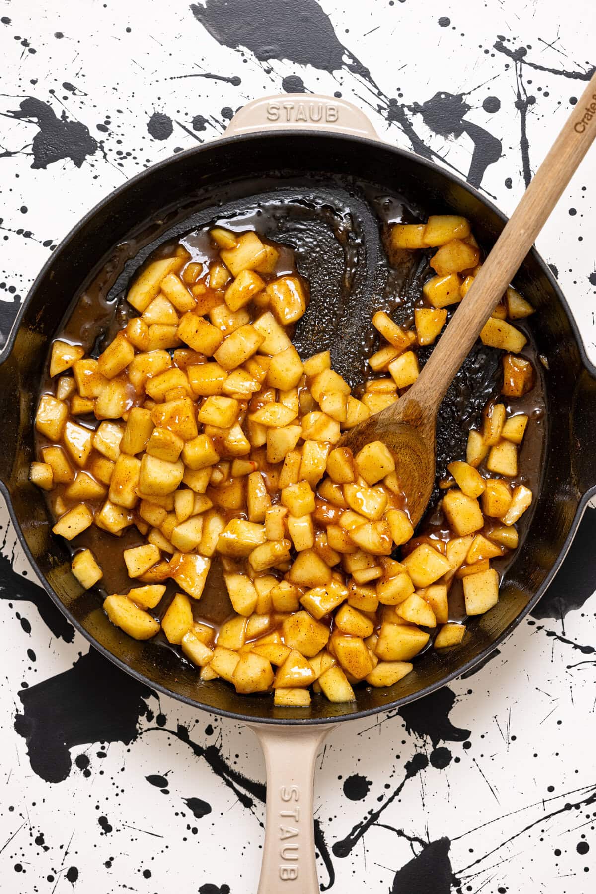 Sautéed chopped apples in a skillet with a wooden spoon.