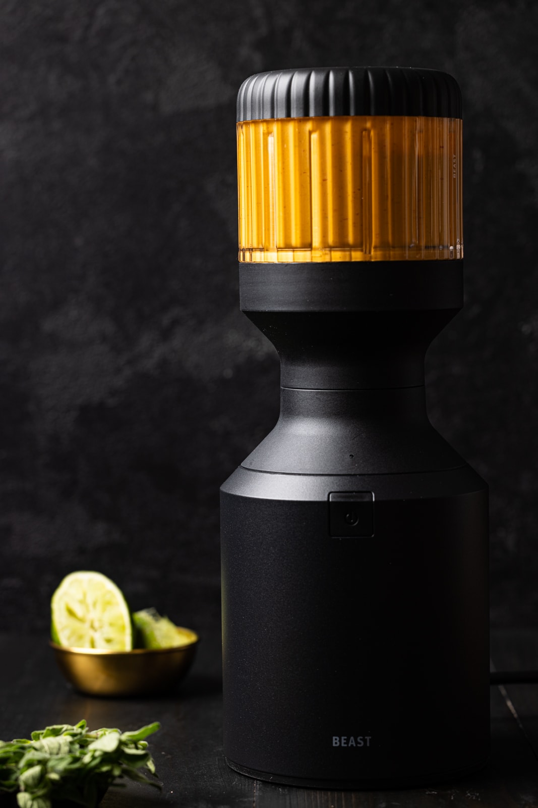 Sauce in a black blender on a black table with herbs and lime.