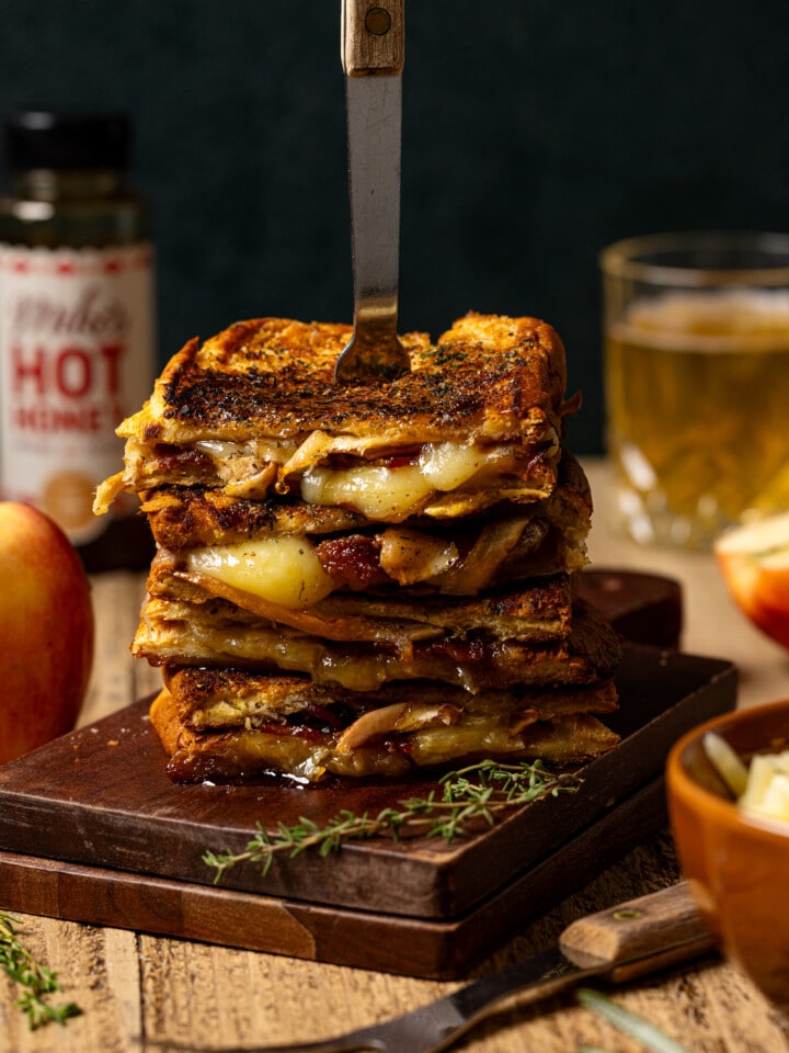 Stack of grilled cheese with apple, hot honey, drink, and bowl of cheese.