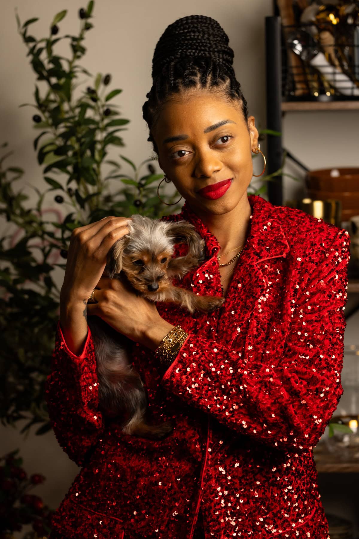 Shanika in a sparkling red suit holding her puppy and smiling.