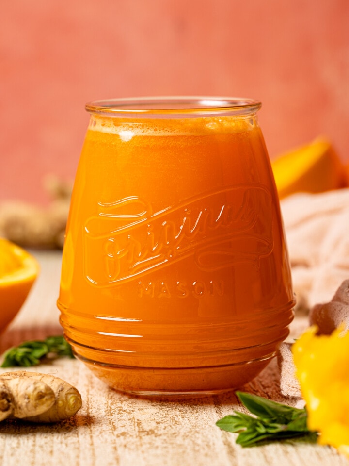 Up close shot of juice in a mason jar with oranges and ginger.