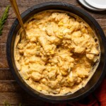 Potato salad in a black bowl with a gold spoon and white plates on the side.