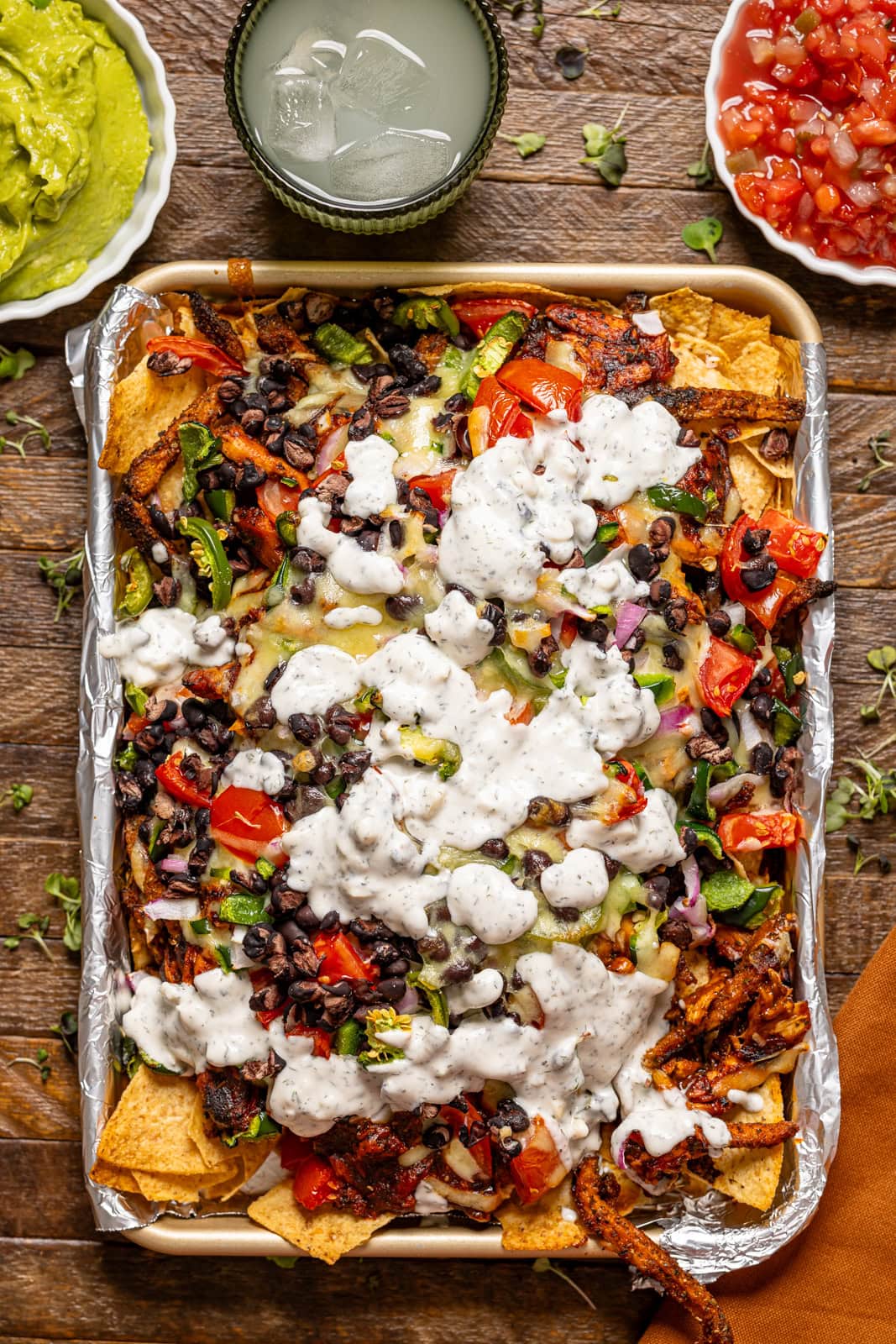 Baked bbq chicken nachos on a baking sheet with a side of drink, guacamole, and salsa.