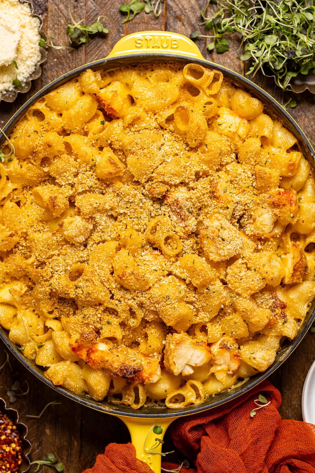 Baked lobster mac and cheese in a yellow skillet on a brown wood table.