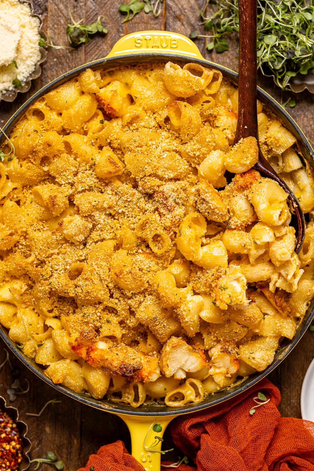 Baked lobster mac and cheese in a yellow skillet with a wooden spoon.