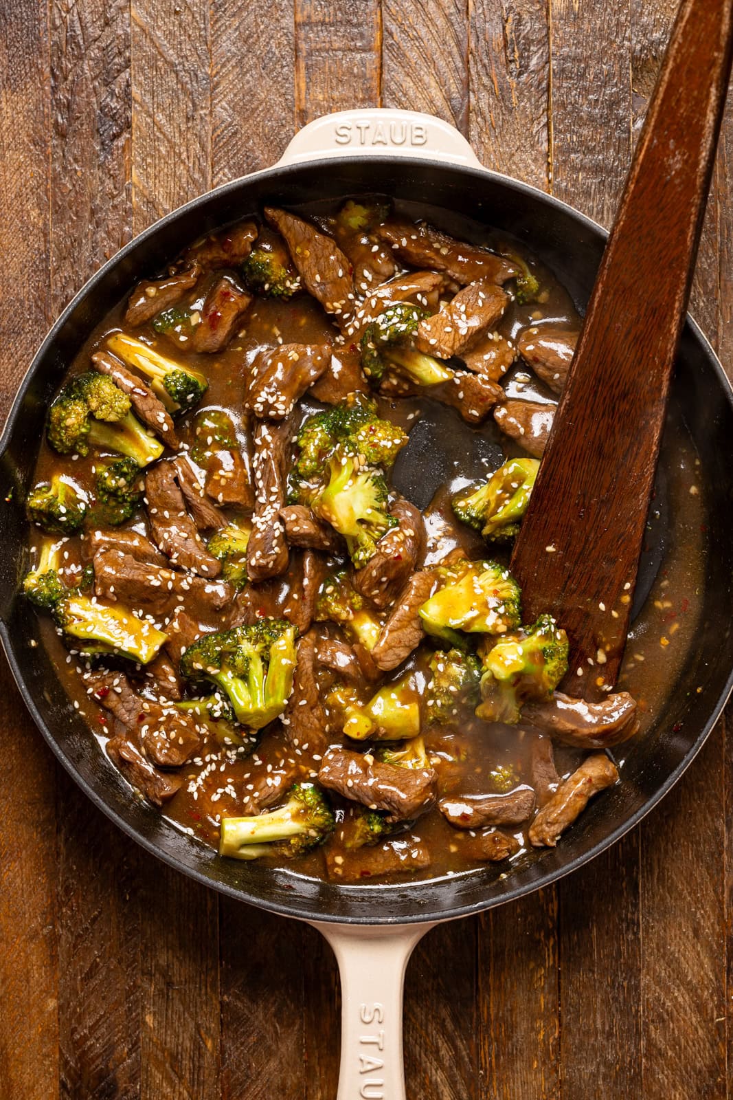 Cooked beef and broccoli in a white skillet with a wooden spoon.