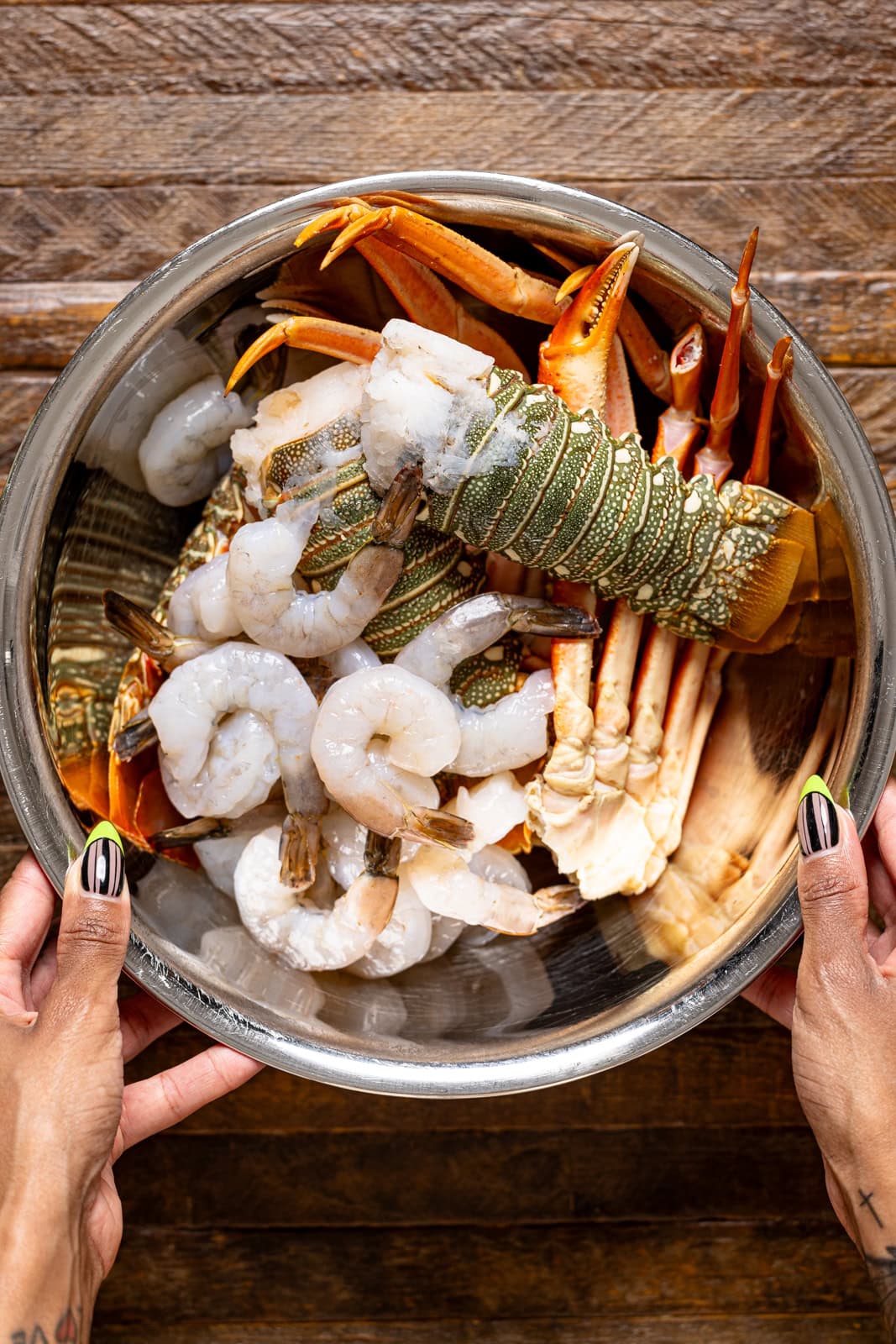Seafoods in a silver metal bowl being held.