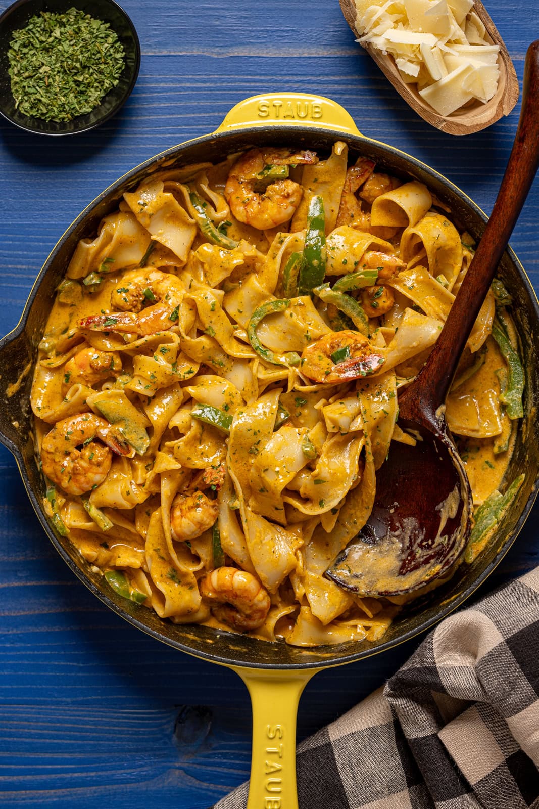 Shrimp pasta in a yellow skillet with a wooden spoon on a blue wood table.